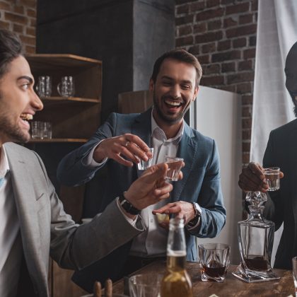 smiling multiethnic male friends in suits drinking tequila together