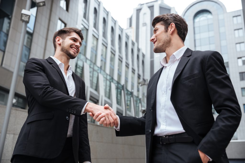 Two happy businessmen standing and shaking hands near business center